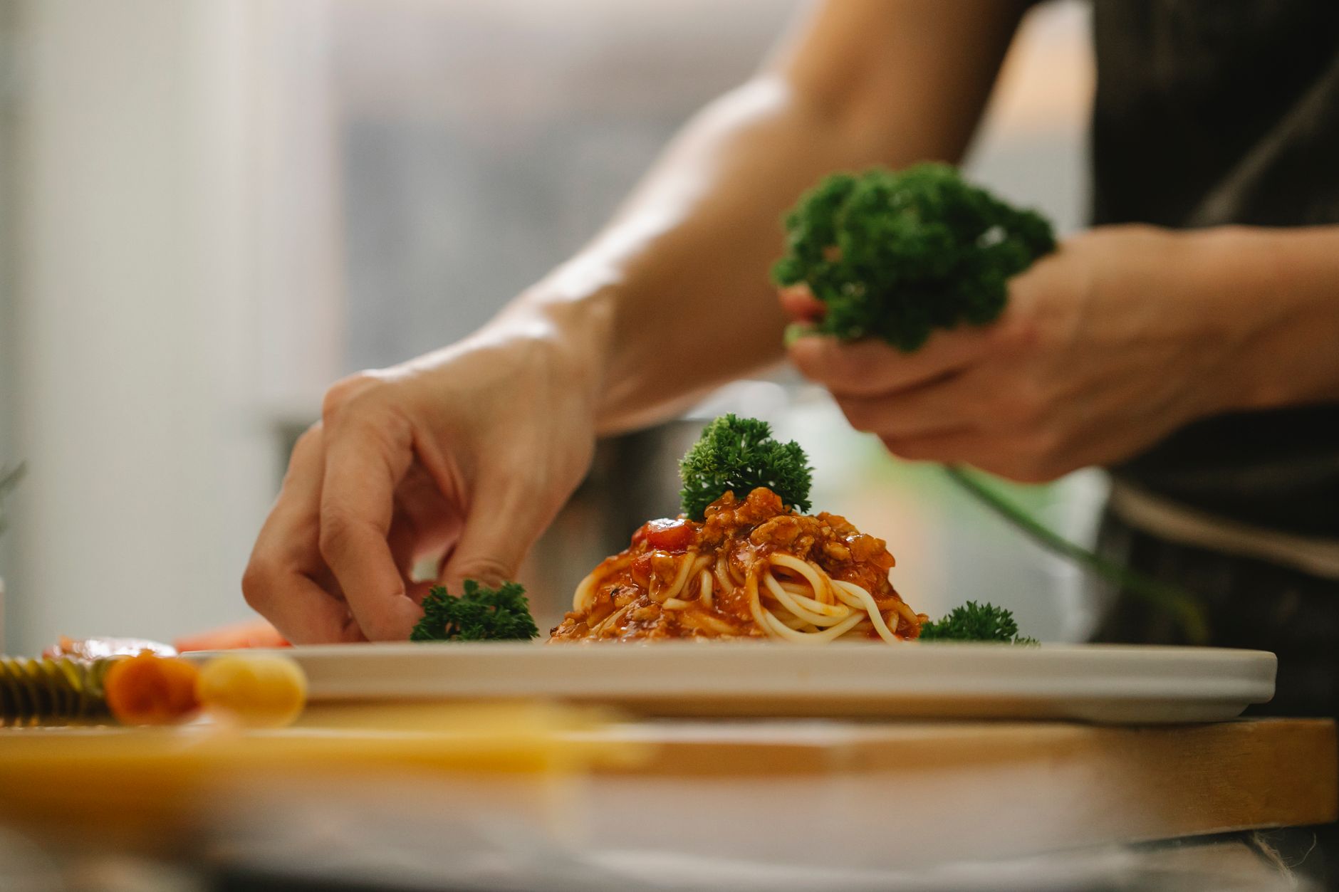 Crop anonymous housewife adding ripe parsley on delicious spaghetti with tomato sauce while cooking in kitchen — Empowering C