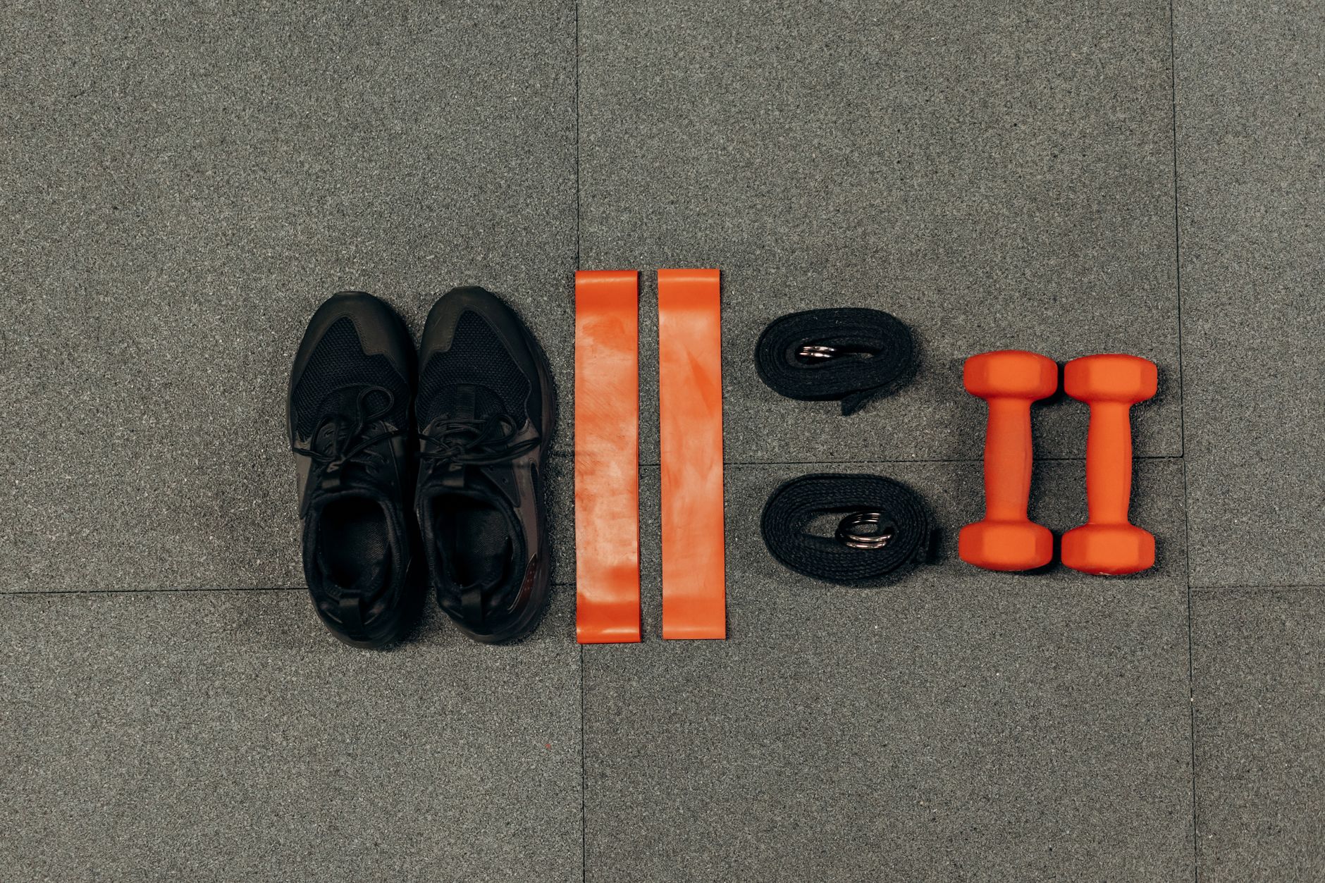 Flat lay of gym essentials including dumbbells, sneakers, and resistance bands on a grey floor. — Join an EMS Fitness Studio